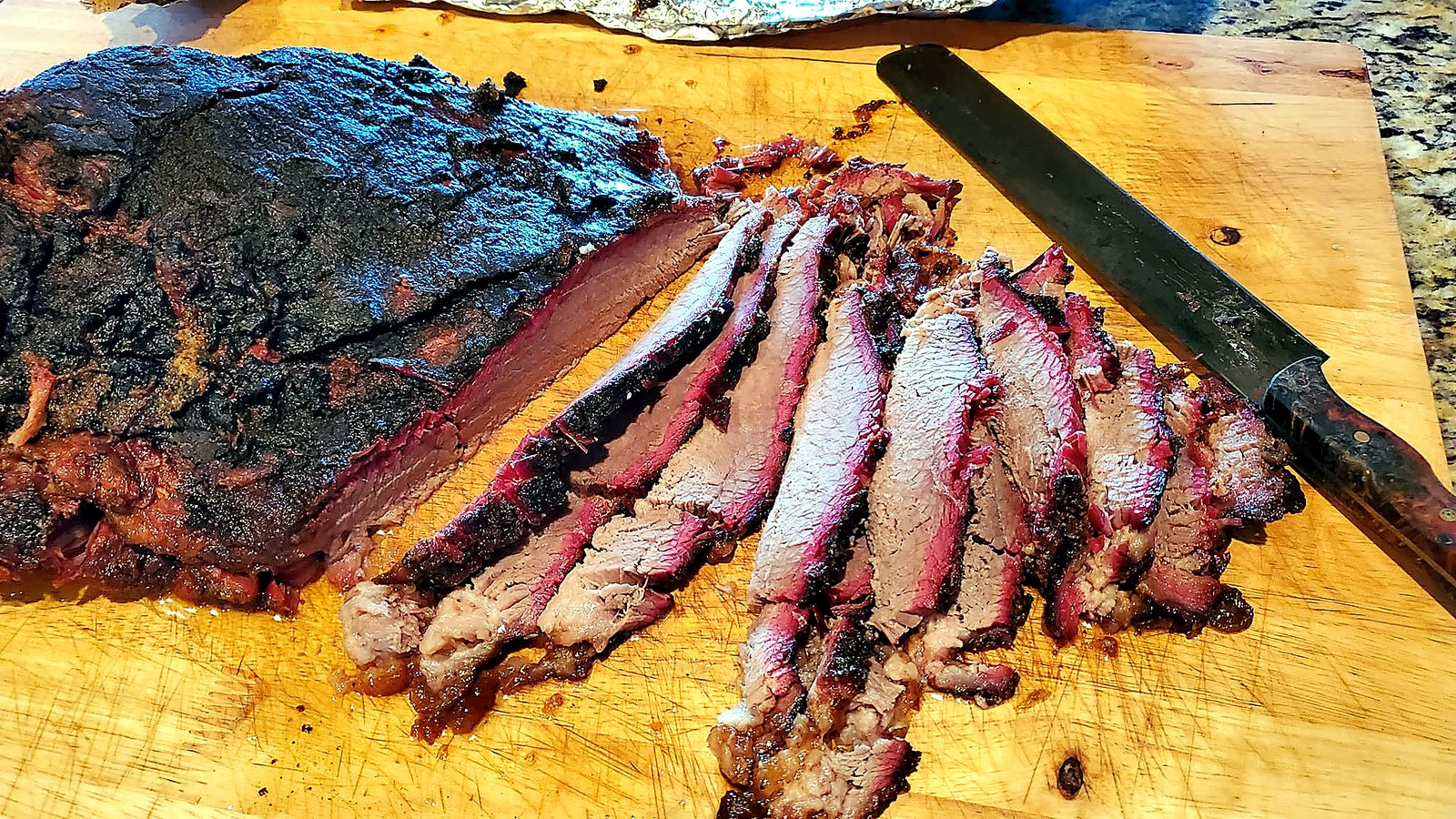 Smoked beef brisket sliced across a cutting board, showing the bark and pink smoke ring.
