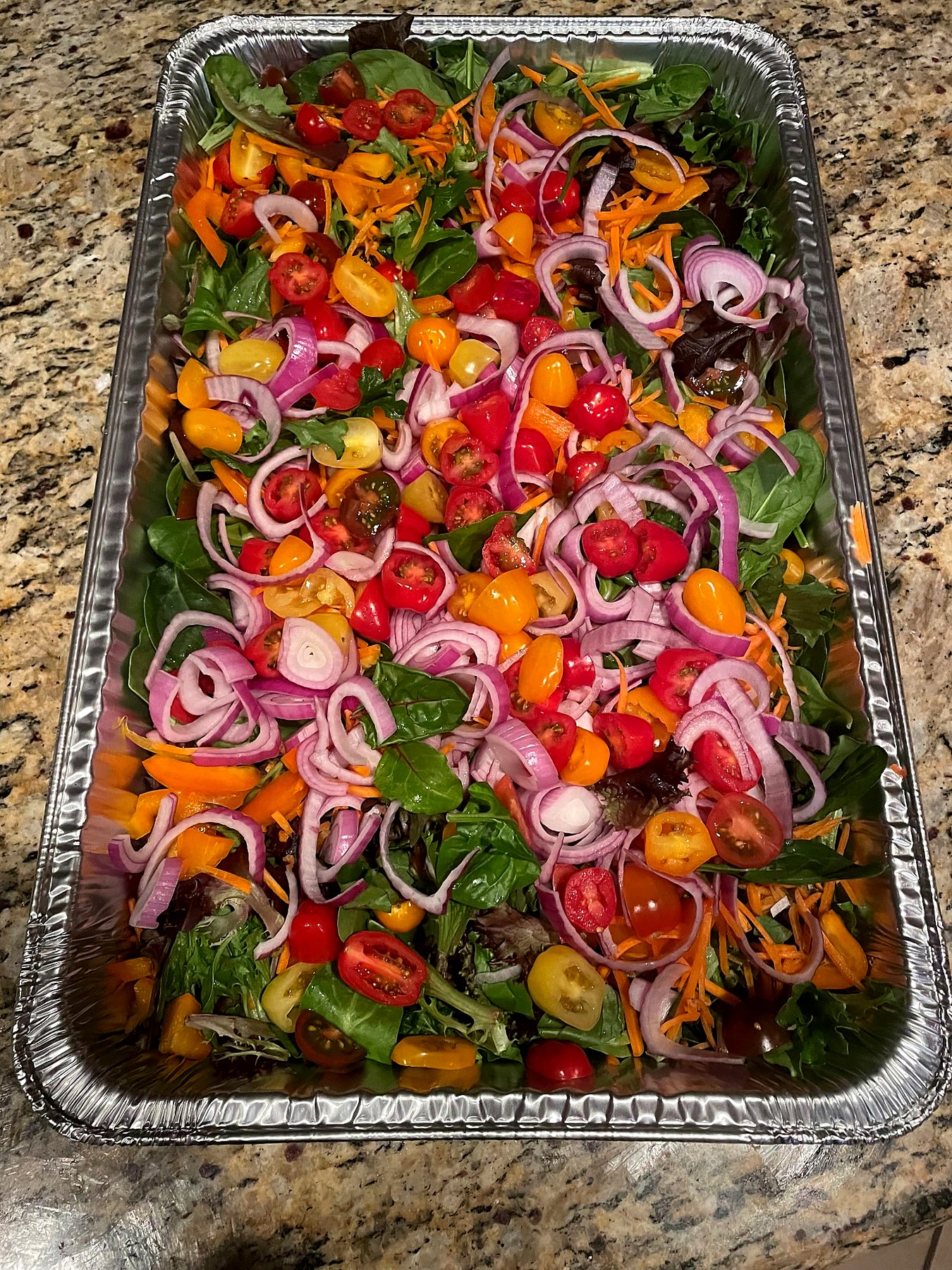 Fresh catering salad with mixed greens, colorful cherry tomatoes, carrots, and sliced red onion.