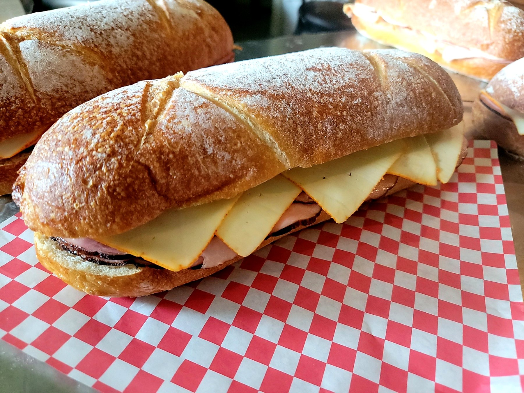 Catered deli sandwiches with sliced meat and cheese on crusty rolls over red and white deli paper.
