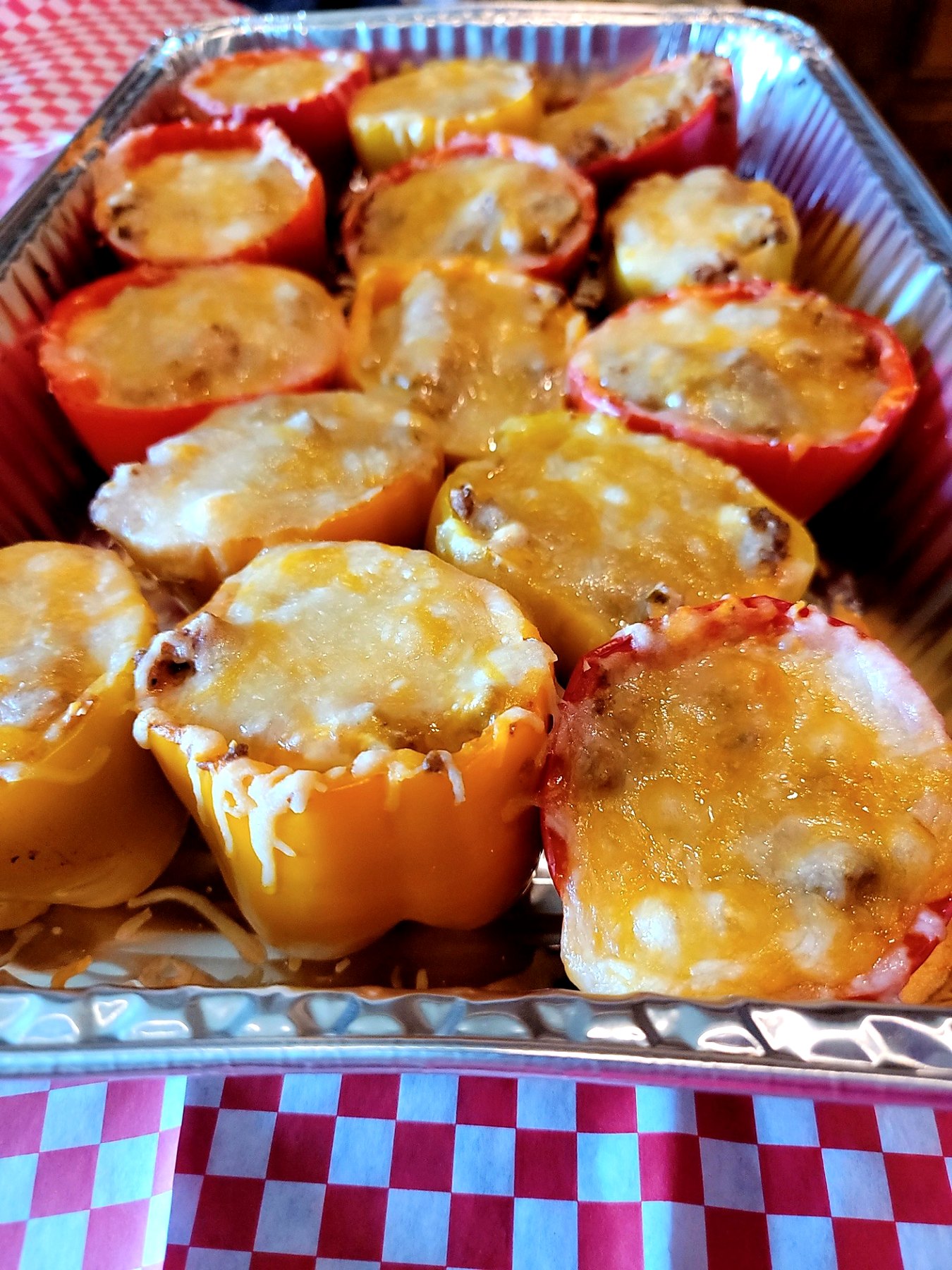 Tray of red and yellow stuffed peppers baked with melted cheese on top.