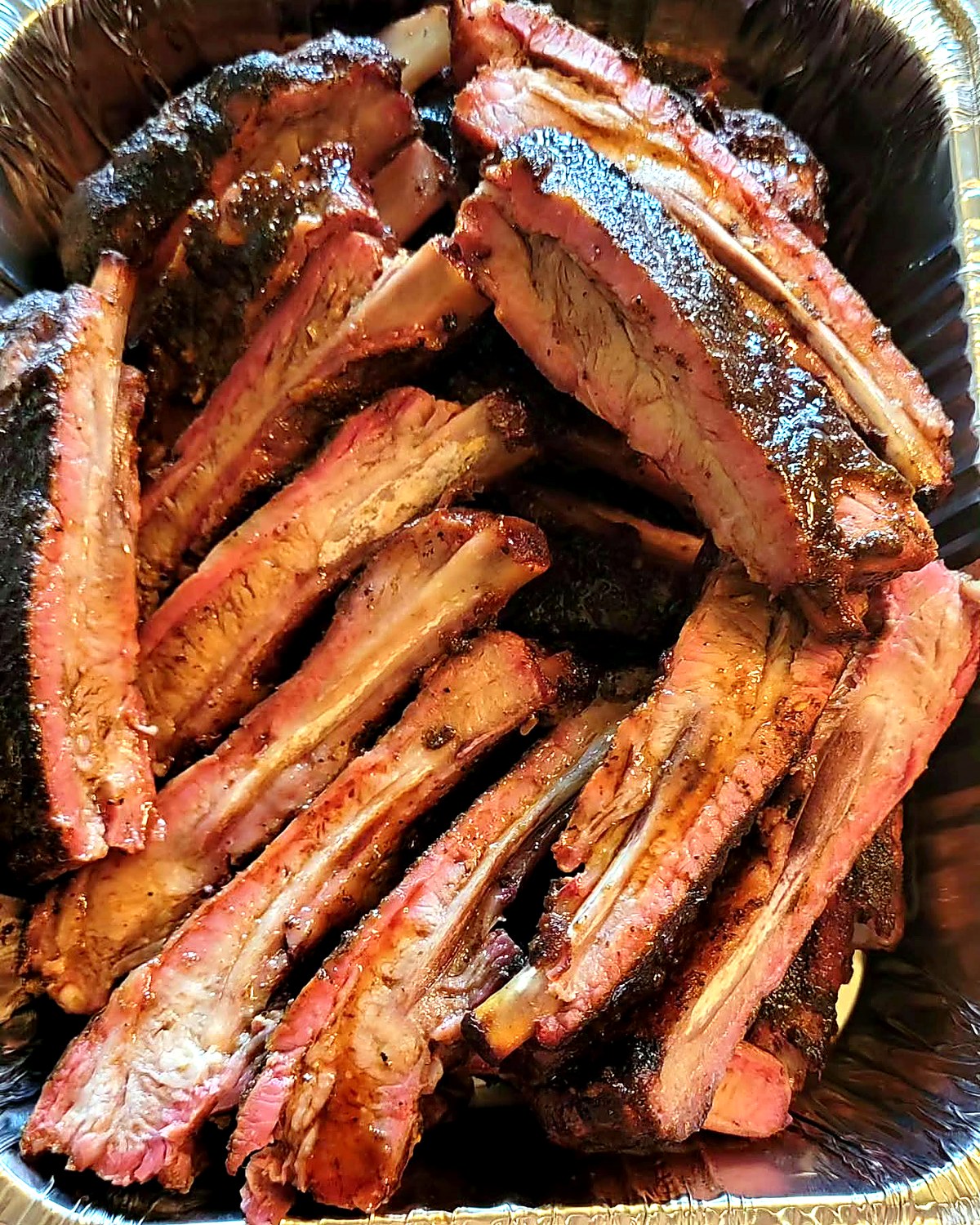 Close view of freshly smoked ribs in a serving tray, with seasoned bark and visible rib bones.